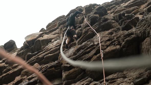 A Male Climber Insures a Rope Climbing a Rocky Route in the Rain
