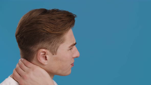 Young Man Suffering From Neck of Pain Massaging It Profile Portrait Blue Studio Background alt