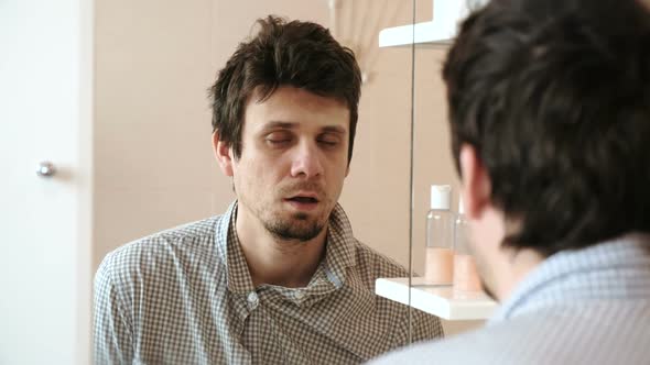 Tired Man Who Has Just Woken Up Looks at His Reflection in the Mirror Almost Asleep Standing Up