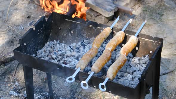 Sausages on Skewers are Cooked on the Portable Grill Outdoor Close Up BBQ alt