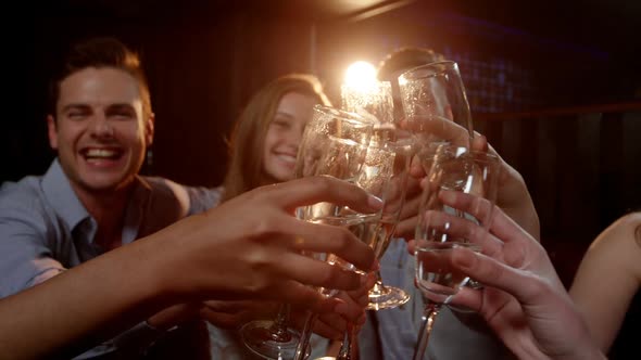 Group of smiling friends sitting on sofa and toasting a glasses of champagne alt