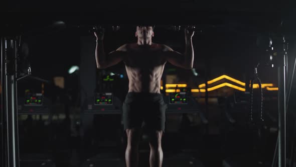 Wellness Athletic Man Performs Pullups on the Horizontal Bar Strength Training in the Gym at Night alt