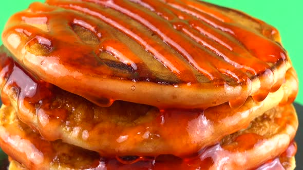 Pancakes with strawberry topping on a green background. Pancake lies on a black slate round stone. alt