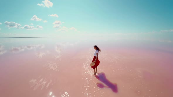 Slow Motion of Laughing Happy Woman Traveler in Red Skirt and Hat Walking in Pink Water with alt