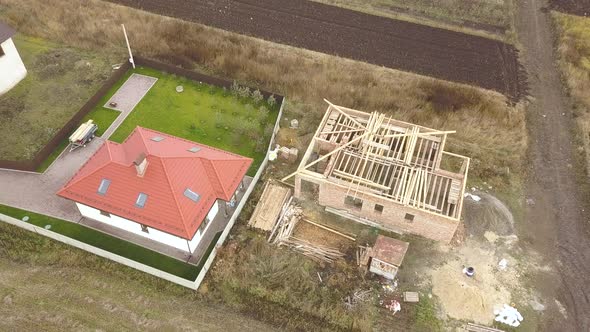 Top Down Aerial View of Two Private Houses One Under Construction with Wooden Roofing Frame and alt