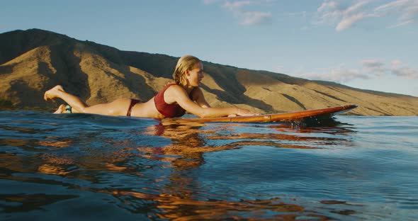 Beautiful woman paddling out to surf at sunset alt