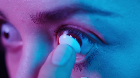 Closeup of a Browneyed Young Woman Putting on the White Decorative Lens with Fingers in Ultraviolet alt