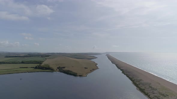 Aerial tracking forward looking east along the fleet lagoon and chesil beach at Abbotsbury. On the h alt