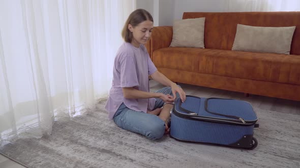 A Woman Closes a Suitcase with Clothes Sitting on the Floor Preparing for the Trip