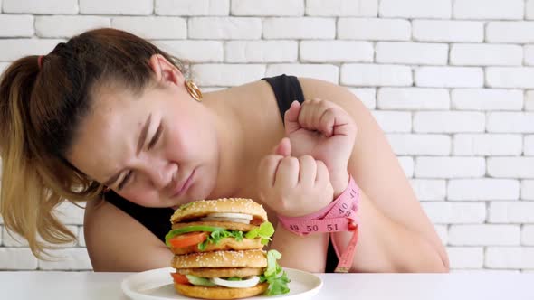 Overweight woman tied her hands with measuring tape and restraint do not to eat hamburger alt