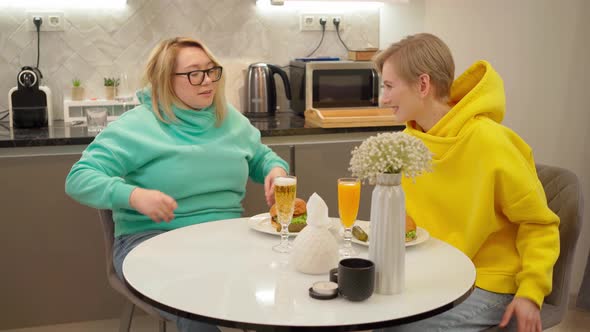 Lgbt Couple in Colored Sweatshirts Sit Down to Eat at the Table and Kiss alt