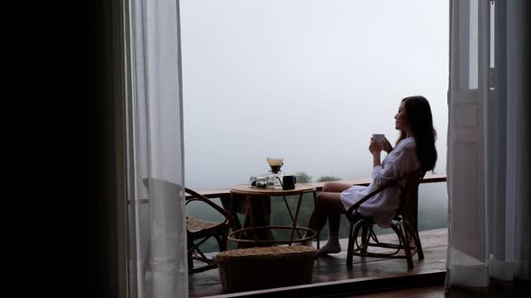 A woman drinking drip coffee and enjoy watching a beautiful nature view on foggy day