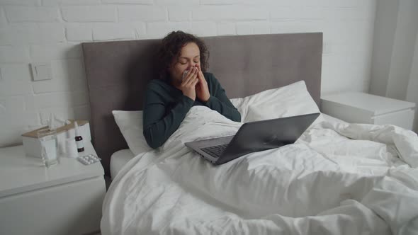 Sick Adult Woman Lying in Bed Watching Video Movie on Laptop Indoors alt