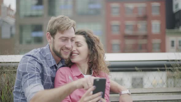 Couple sitting together in park looking at smart phone alt
