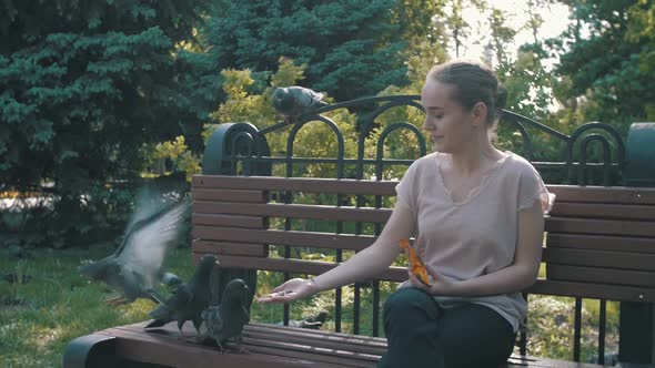 Young Happy Girl Feeding Pigeons in the Park on a Bench