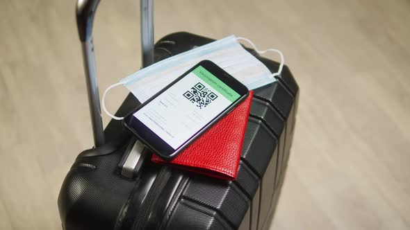 QR Code on Smartphone Medical Mask and Passport on Suitcase alt