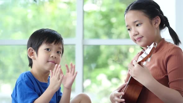 Asian Children Playing Ukulele Together In Living Room alt