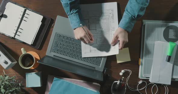 Office worker checking paperwork and using a laptop