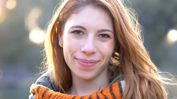 Attractive young woman with red hair smiling at camera in the park alt