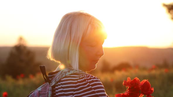 Adult Caucasian Woman Tourist with Backpack and Poppy Flower Bouquet at Sunset in the Field