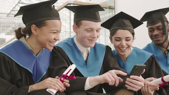 Four Young Graduates Looking at Telephone Screen and Laughing alt