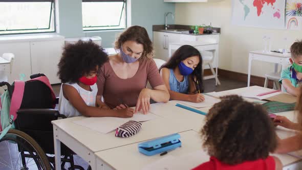 Female teacher wearing face mask teaching a disable girl in class alt