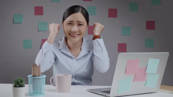 Asian woman working looking at camera and make winning gesture.