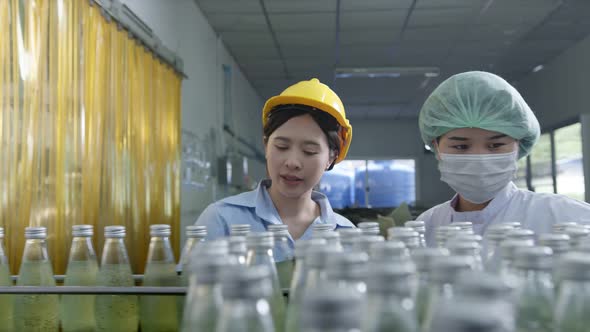 Asian Female supervisor inspecting bottle of herb drink production line alt