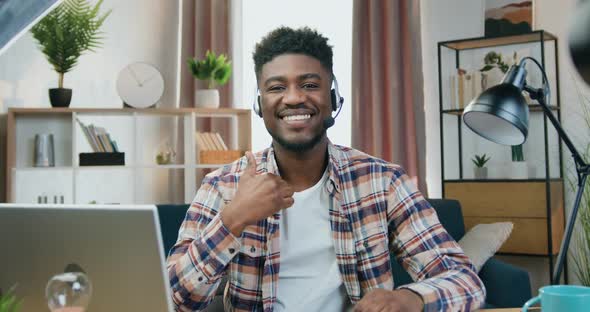 African American Guy in Headphones with Mic Sitting in front of Camera in Home alt