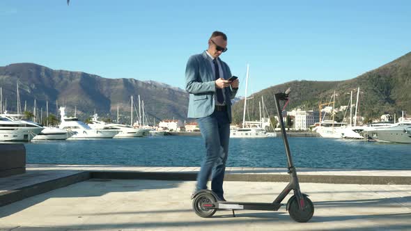 Handsome Business Guy Unlocks the Electric Scooter Using the Application on a Smartphone and Leaves