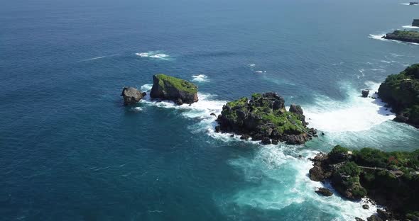 Aerial view showing blue colored ocean waves crashing against coral rocks at Timang Island,Indonesia alt