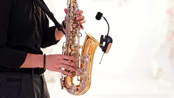 Saxophonist in black shirt and trousers plays jazz on golden saxophone with microphone.  alt