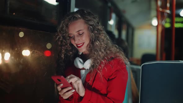 A Smiling Curly Woman is Using Smartphone and Reading Messages in Bus alt