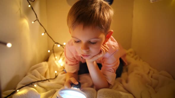 Dolly Shot of Cute Boy Reading Book While Playing in His Toy House at Night alt