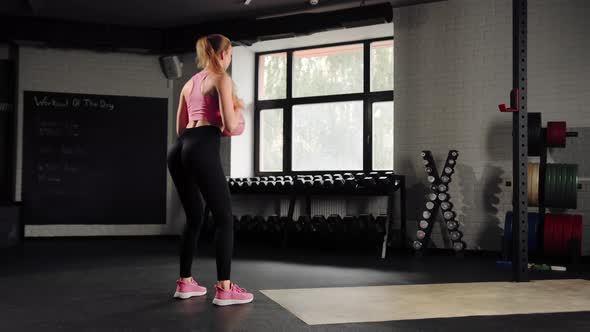 Attractive young beautiful woman doing cardio exercise and squatting with kettlebell in gym alt