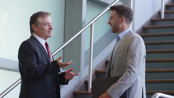 Two businessmen meet and shake hands on stairs of office lobby