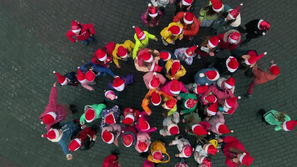 Many happy kids with Santa Christmas hats jumping on the square. Slow motion Top down aerial view. alt