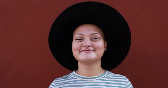 Hipster bald girl smiling on camera outdoor in the city with red background alt