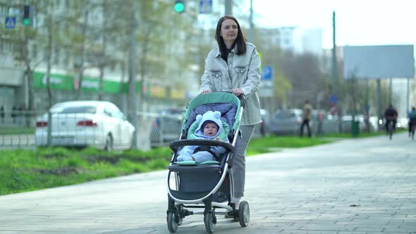 Woman Walks with Baby Stroller in Which Child Boy is Sitting