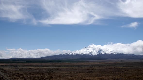 Wide establishing shot of Mount Ruapehu surrounded by beautiful clouds in New Zealand. alt