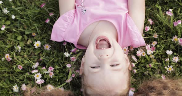 Close-up Smiling Little Cute Baby Girl Lying on Green Grass Holding Flowers Looking at Camera