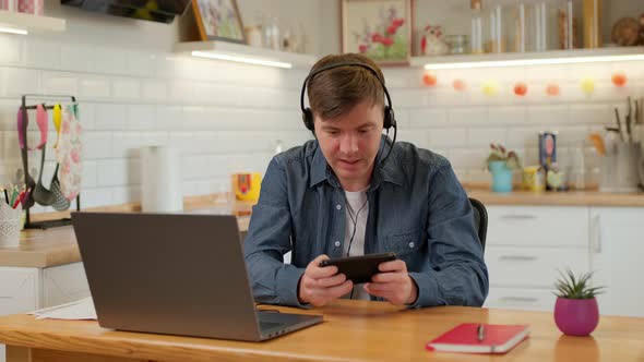 Happy man is playing video game at home using modern smartphone touching screen alt