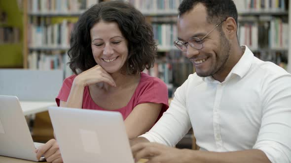 Cheerful Colleagues Sitting at Library and Communicating alt