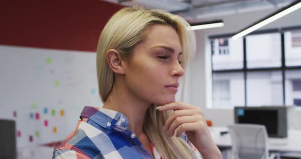 Caucasian businesswoman rubbing her chin in thought and smiling in office alt