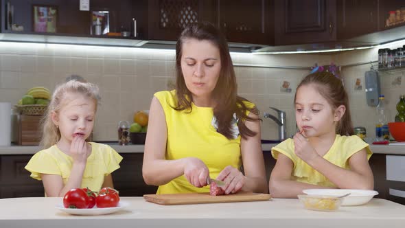 Mom and Children Cook in the Kitchen. Little Girl Smooths Pizza Dough. Mom Helps Children Cook Pizza alt