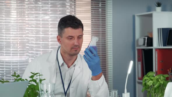 Handsome Research Scientist Observing the Liquid Reaction in Conical Flask During the Experiment alt