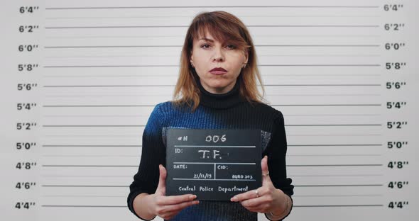 Portrait of Adult Woman with Dyed Hair Holding Sign for Photo in Police Department alt