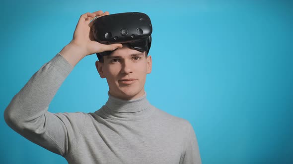Smiling Guy with Virtual Reality Headset Poses at Blue Wall alt