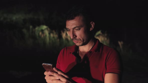 A Young Male Criminal Hiding at Night in the Forest Speaks on the Phone Online alt