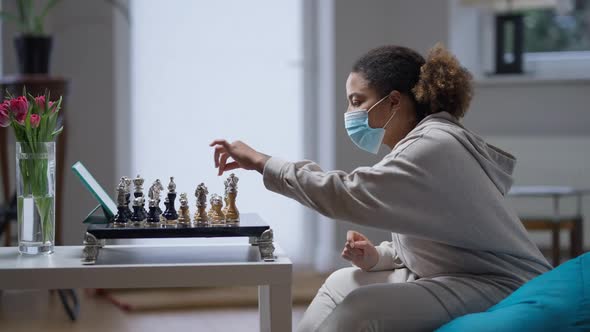 Side View of Young African American Intelligent Woman in Coronavirus Face Mask Playing Chess in alt
